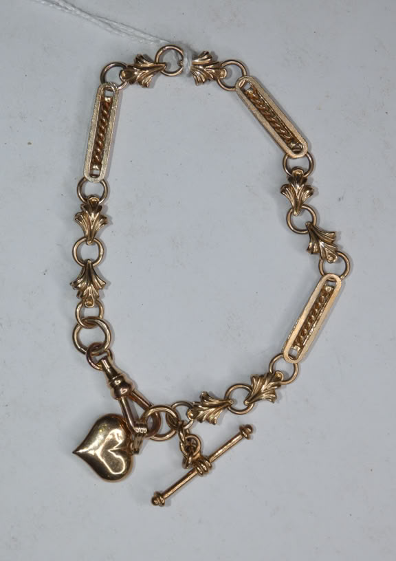 A gold bracelet with circular links, rectangular engraved plates, and a heart-shaped charm.