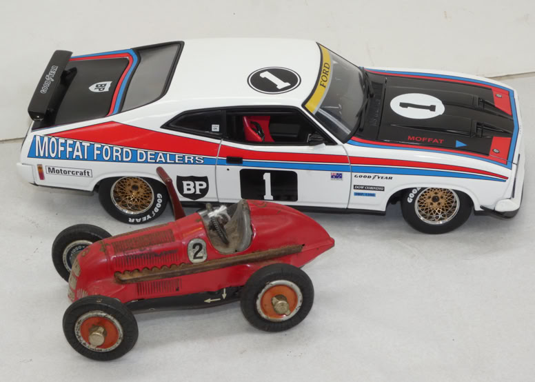 Two toy cars on a surface: a larger white, black, and blue car with racing decals, and a smaller red car with a number on the side.