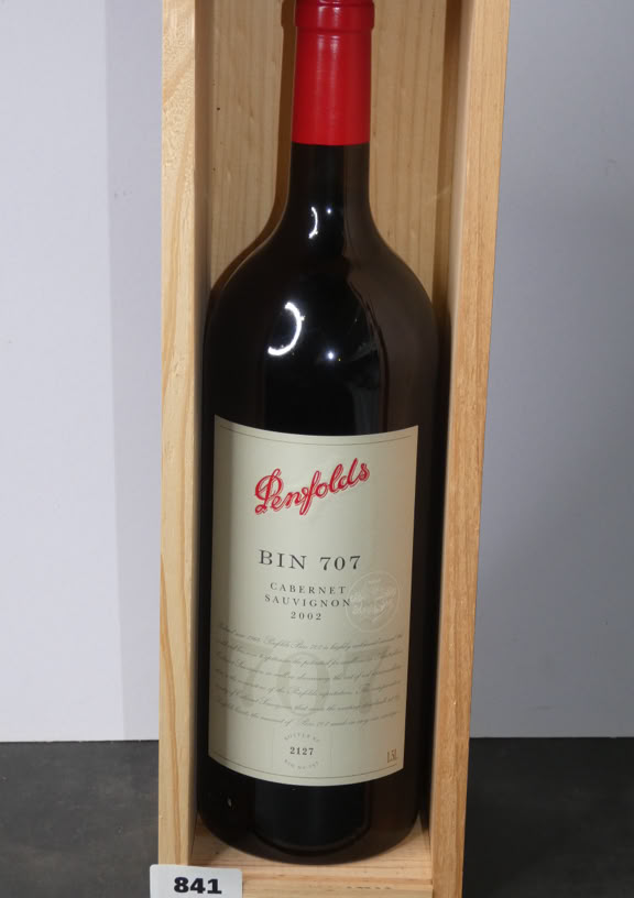 A wine bottle with a red cap, labeled "Penfolds Bin 707," placed inside a wooden box.